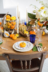 Luxurious elegant wedding decor in autumn style. Wooden vintage table and chairs setting with ceramic plates and silver cutlery. Fresh flowers in a vase, orange pumpkins, deer horns and candles.