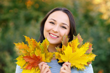 Portrait of smiling young woman with autumn leafs in front of foliage
