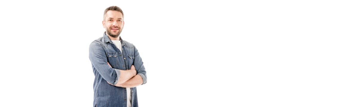 panoramic shot of smiling bearded man in denim shirt standing with crossed arms isolated on white