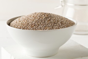 Whole, organic white chia seeds heap in white bowl on white table background