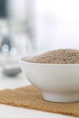 Whole, organic white chia seeds heap in white bowl with bright kitchen background - selective focus