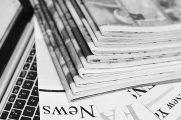 Newspapers and laptop. Pile of daily papers with news on the computer. Pages with headlines,...