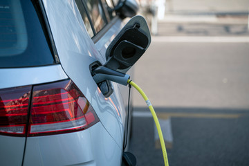 Electric Car silver color - plugged in for charging. charging station for electric car. Close up of the power supply plugged into an electric car being charged. Car charging cable.