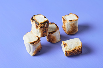 Scattered and grilled white sugary marshmallows cylindrical form lies on purple scratched concrete table. Close-up