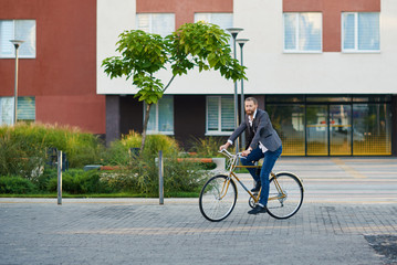 Fototapeta na wymiar Bearded Businessman in business suit riding on retro bicycle to work on urban street in the morning on sunset