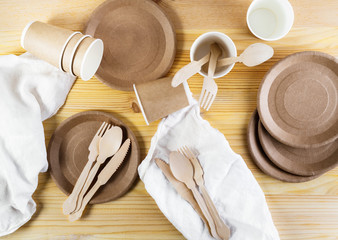 Brown paper cups, plates, wooden cutlery, linen napkins on wooden background. Recycling concept.