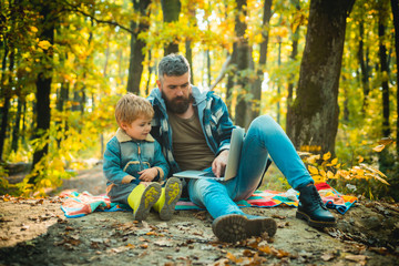 Fototapeta premium Father playing with little son on a picnic in the park in early autumn day. Cute little boy with his father during stroll in the forest.