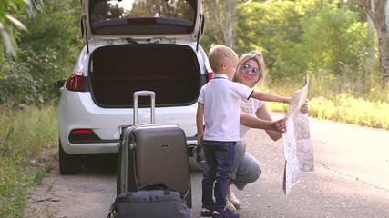 Young active mother and son traveling by car, they stopped on the road and look at the route on the map. Portrait of a family of tourists with a map near the car with an open trunk. Slow motion.
