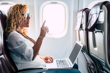 Beautiful female passeger of airplane use personal laptop computer on board with wifi internet connection and ask for hostess help - travel for business modern people concept