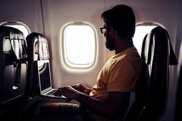 Adult bearded traveler man sitting inside the aircraft and flight to destination - computer with wifi internet connection on board service concept - traveler people fly lifestyle