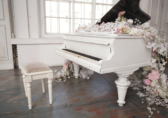 white grand piano with spring white and pink flowers in a white room with nobody