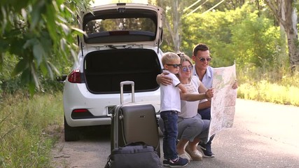 Young family looking at map near the car outdoors. Family traveling by car and using paper map to navigate sitting by the car with the trunk open.