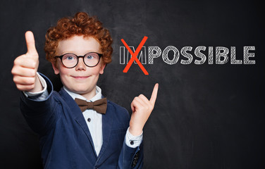 Happy smart child pointing at possible inscription on chalkboard background. Success and develop...