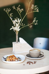 Cup of coffee and plate of belgian waffles on light wooden table in cafe
