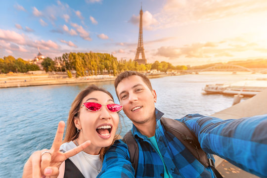 A happy couple in love a man and a woman embrace and take a selfie on the banks of the Seine river with the Eiffel tower in the background. Travel and vacation in Paris and France