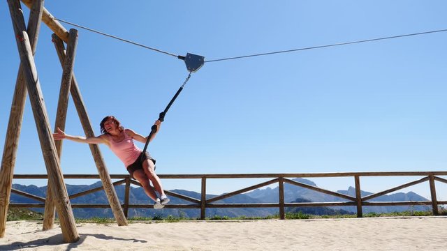 Adult freedom woman tourist having fun on zipline, descend on rope, cable aerial ropeslide. Mountains rest area place in Spain Alicante region. Costa Blanca holiday