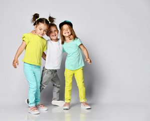 Studio portrait of children on a light background: full body shot of three children in bright clothes, two girls and one boy. Triplets, brother and sisters.