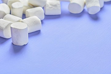 Lot of scattered white marshmallows cylindrical form lies on purple scratched concrete table. Space for text