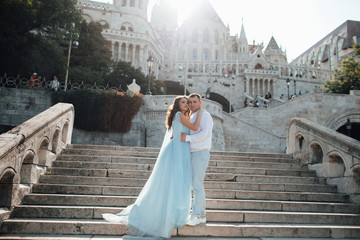 Attractive couple in love in elegant glamour outfit stand on the stairs. Pretty woman with makeup...
