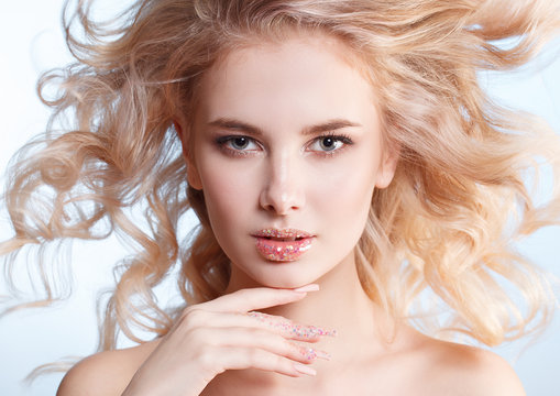 close-up portrait of beautiful curly blondy woman with perfect art make-up, trendy frosted nail design with glitter. Wind in her hair.