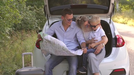 Happy happy parents with a young son traveling by car, mom playing with her son and dad studying the route map. Summer trip outside the city in the countryside.