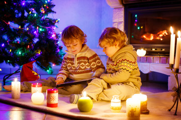 Two cute toddler boys, blond twins playing with new tablet gift. Family celebrating Christmas holiday