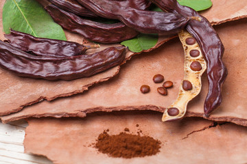 Carob. Organic carob pods with seeds and leaves on tree bark table. Healthy eating, food background.