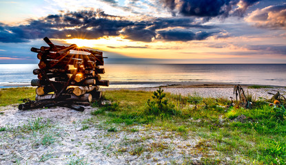 Fototapeta premium Coastal landscape with pile of wood and fishing anchors on sandy beach of the Baltic sea at dawn