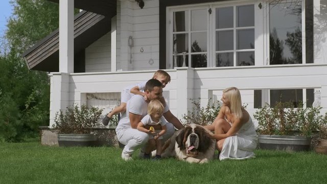 A young family of four and a dog having fun sitting near their white house