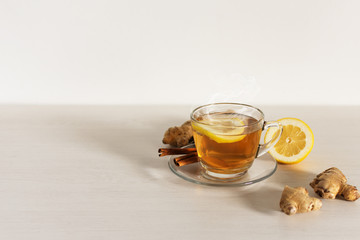 A cup of hot tea with ginger, lemon and cinnamon on white background.