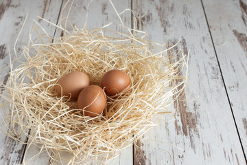 Fresh organic eggs on nest on white wooden background.
