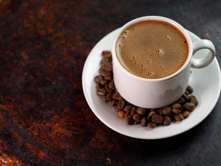 White espresso coffee Cup on rusty iron brown background with coffee beans