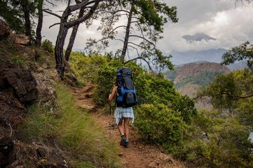 Naklejka premium Girl in the light dress walking up with backpack on the rocks