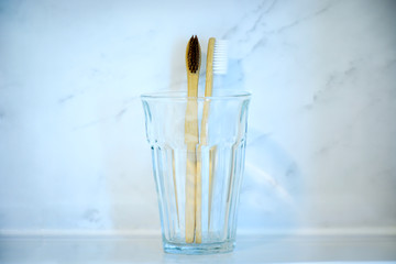 Eco friendly natural wooden toothbrushes in glass standing on sink with marble background in bathroom.