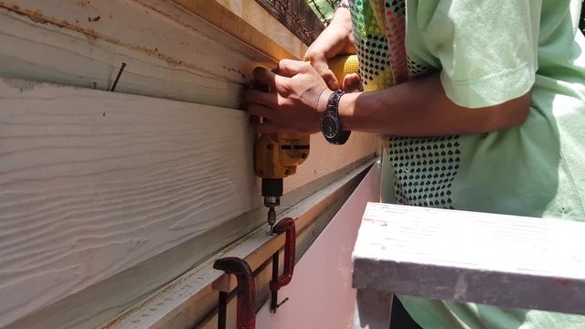 A boy are drilling knot for cling iron fence with a timber blog for renovate the wall