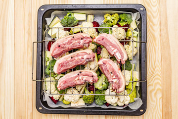 Assorted fresh vegetables on a baking tray. Raw pork belly meat on the grill