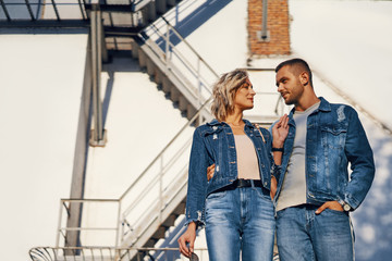 Young beautiful woman and man in jeans cloth posing on urban architecture