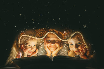 children reading a book under a blanket with light