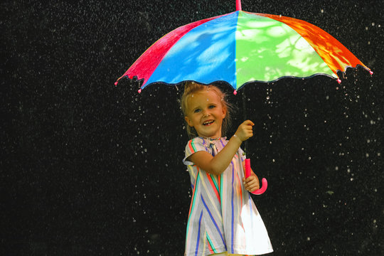 Cute funny  toddler girl holds colorful umbrella playing in the garden by rainy