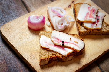 Lard sandwich with black bread and onions on a wooden board.
