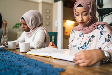 Two young Muslim women study on books at the kitchen table - Arabian Millennials are preparing for university exams