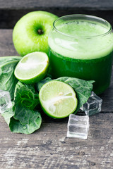 Green apple smoothie in glass and kale leaves on wooden table