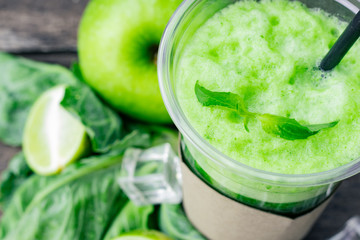 Green apple smoothie in glass and kale leaves on wooden table