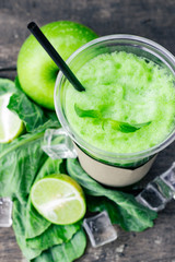 Green apple smoothie in glass and kale leaves on wooden table