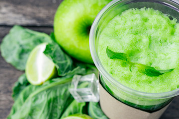 Green apple smoothie in glass and kale leaves on wooden table