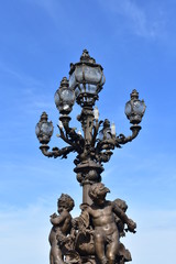 Fototapeta na wymiar Pont Alexandre III detail, bronze streetlight with sculptures and blue sky. Paris, France.