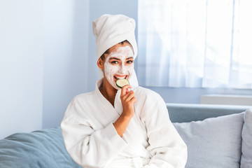 Woman with facial mask and cucumber slices in her hands. Beautiful young woman with facial mask on her face holding slices of fresh cucumber. Young woman with clay facial mask holding cucumber slices