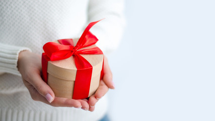 Woman in white sweater holding gift box with red ribbon in hands on white background