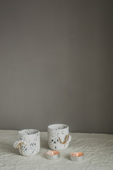 Two white cups on a linen tablecloth with scented candles. Rustic background