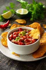 Tasty mexican nachos chips in bowl with salsa dip on wooden table.